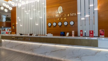 Una recepción de hotel con un panel de pared de madera, relojes que marcan diferentes ciudades y una zona de recepción con mostrador de mármol.