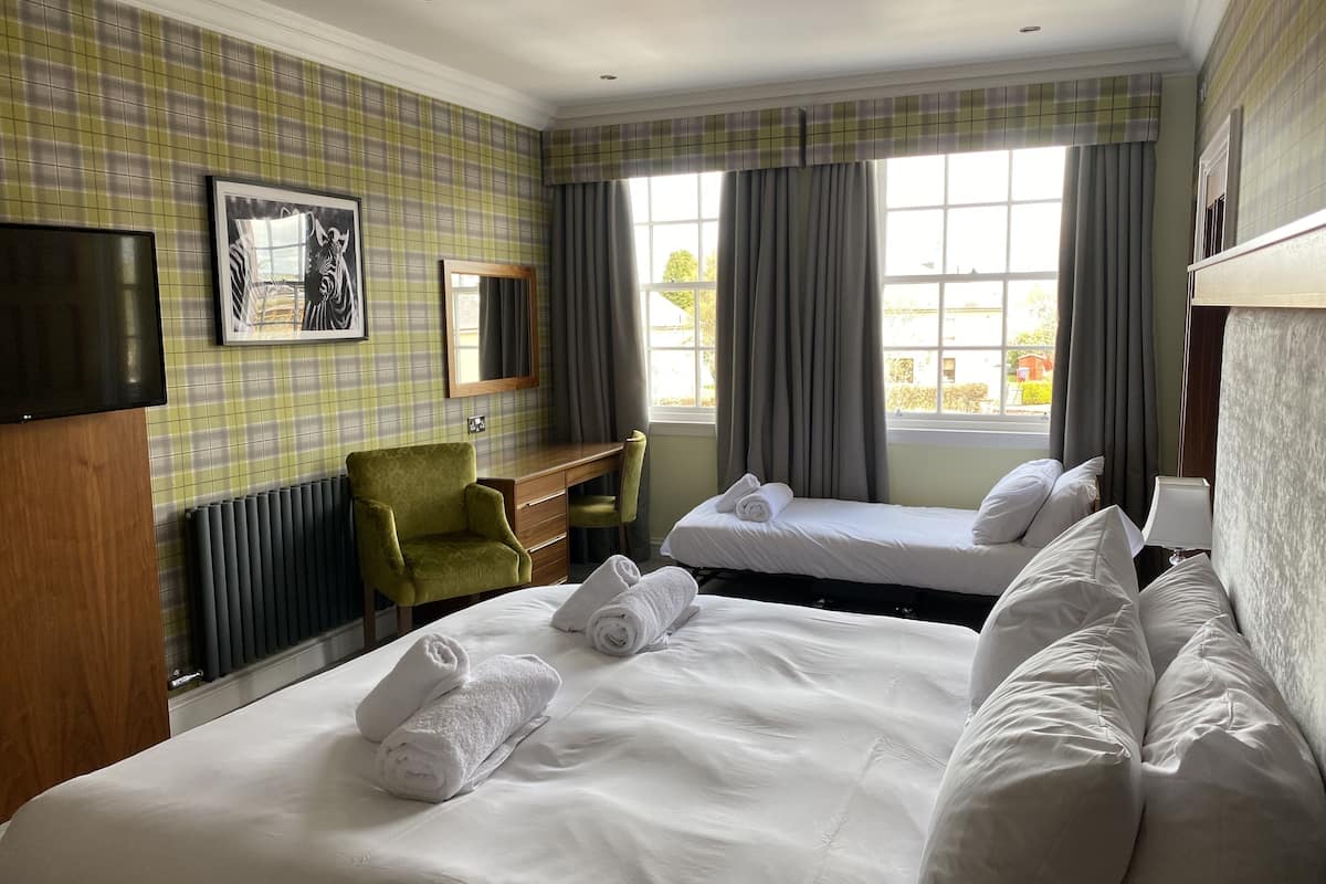 Une chambre d’hôtel avec deux lits, un bureau, une chaise, une télévision et une fenêtre avec des rideaux.