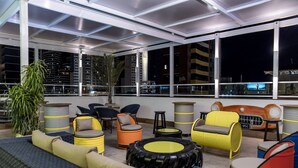 A rooftop lounge with seating areas, a large potted plant, and a view of the cityscape at night. - Hotel Villa Smart (Fortaleza)