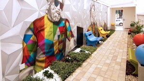 A corridor with a colorful mural, outdoor seating, and a tiled pathway. - Hotel Villa Smart (Fortaleza)