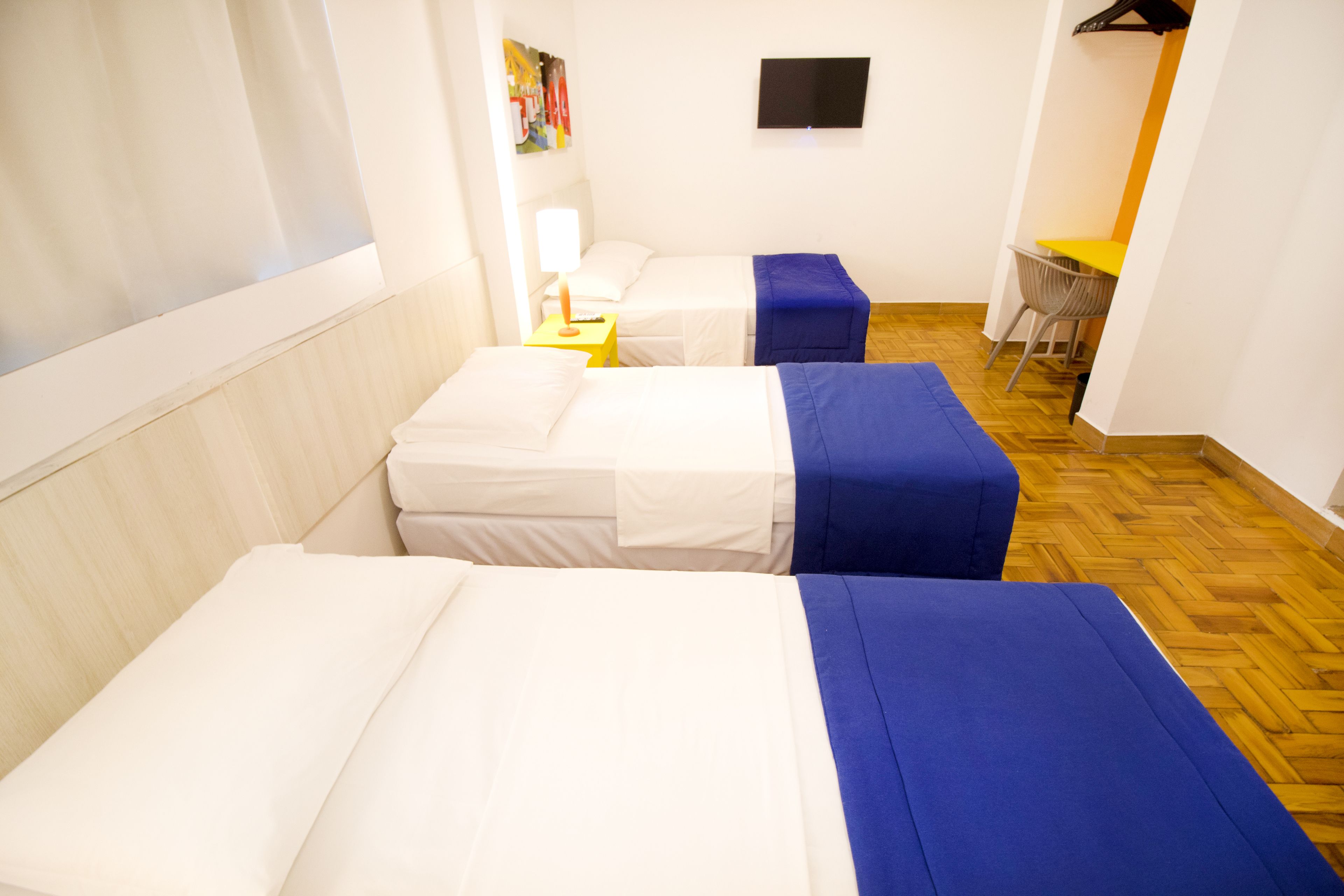 A hotel room with two beds, a TV on the wall, and a small table with a chair.