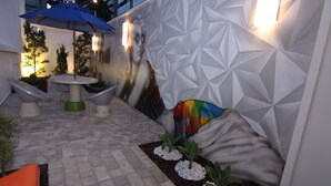 A modern outdoor seating area with a table and chairs, a blue umbrella, and a wall with a geometric pattern. - Hotel Villa Smart (Fortaleza)