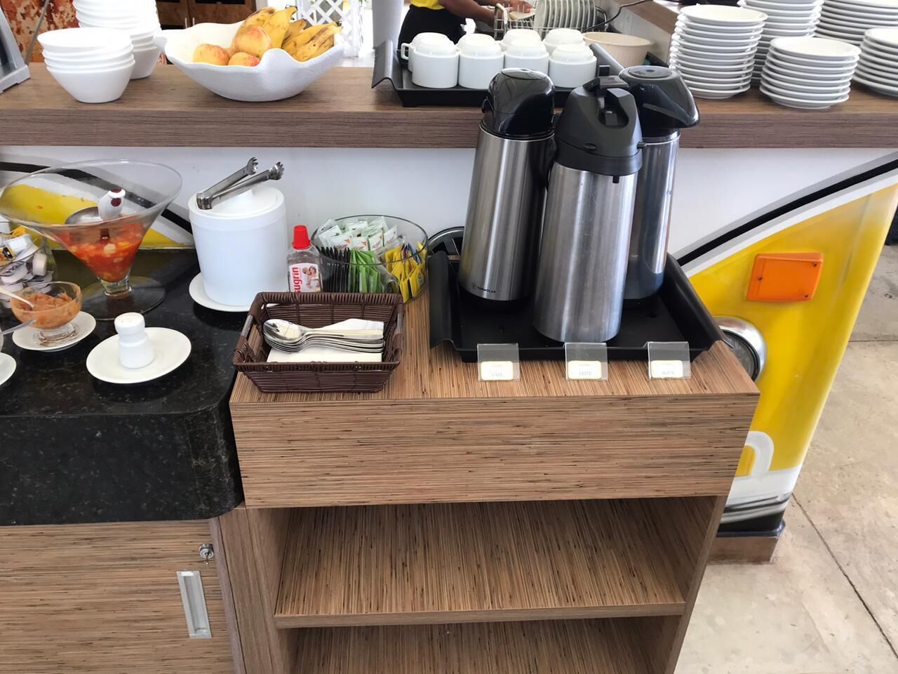 En buffet med forskelligt mad, serveringsbestik og beholdere til varme drikke.