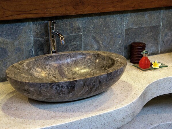 A large, oval stone sink with a modern faucet, set against a tiled backsplash.