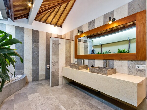A modern bathroom with a large mirror, two sinks, a shower, and a ceiling with exposed beams.