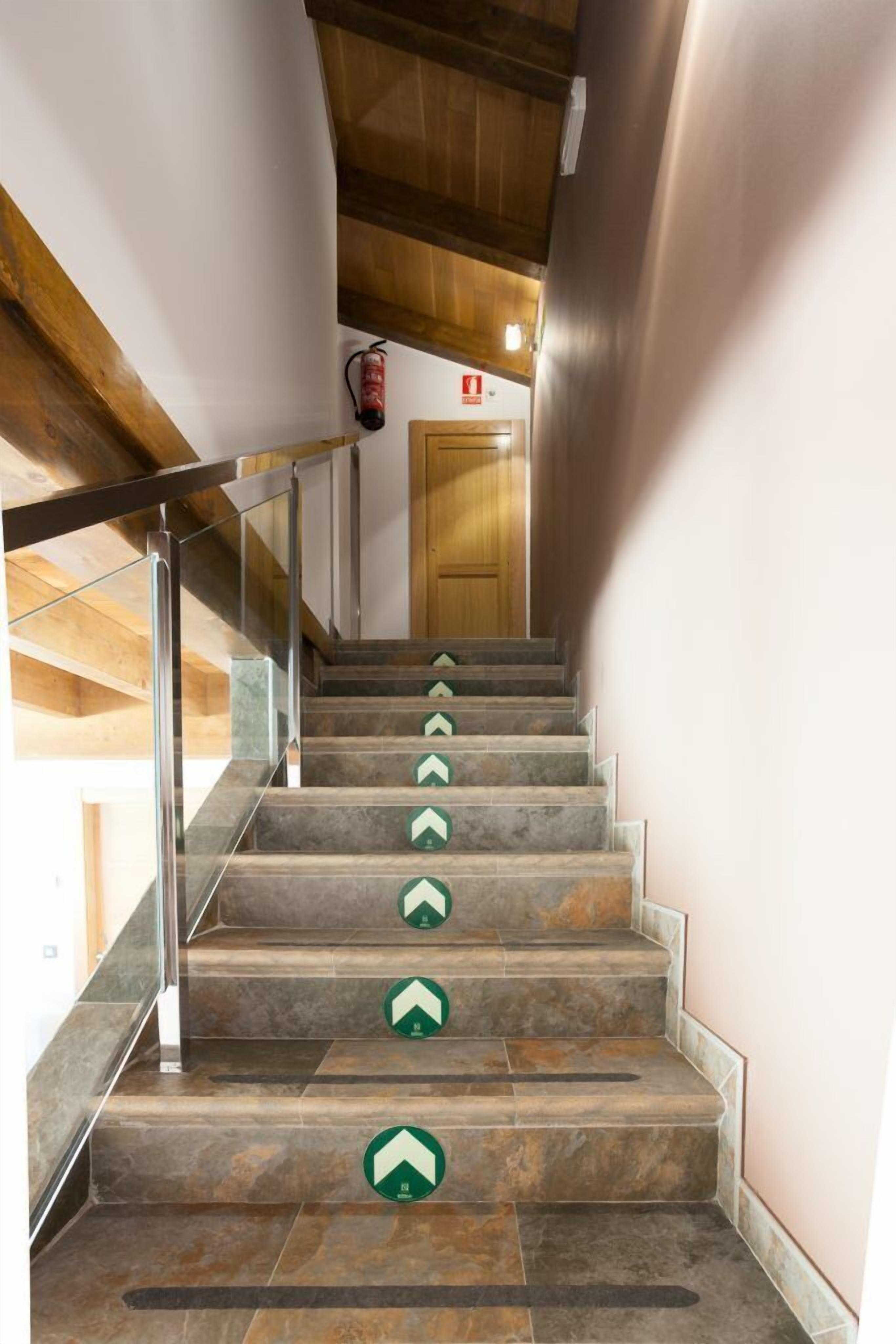 Een trap met pijlen die de richting aangeven, een glazen balustrade en een houten plafond.