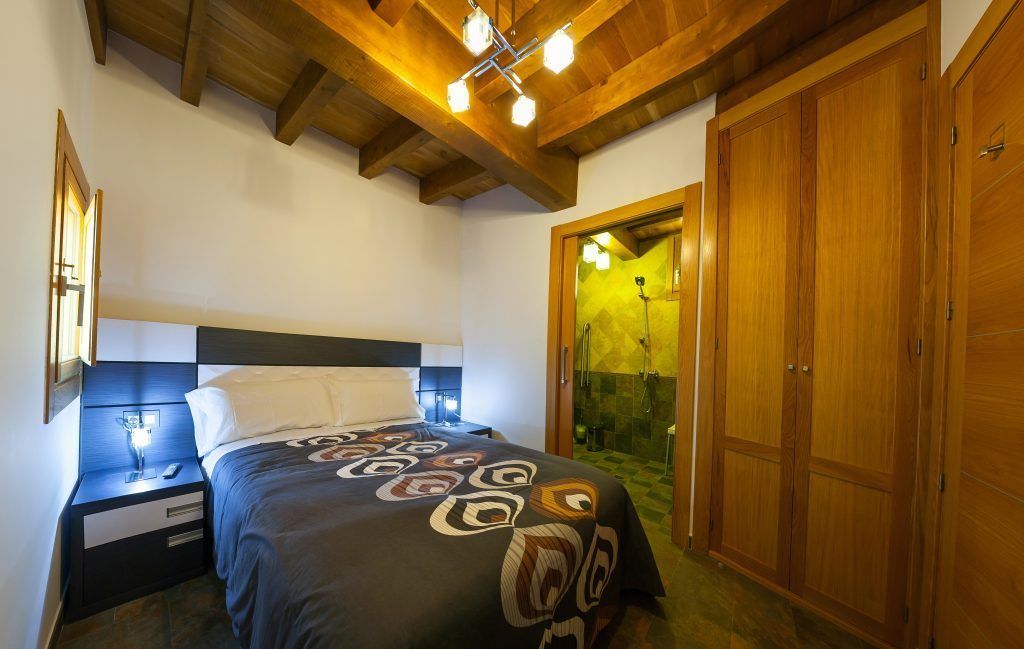 Een slaapkamer met een bed, nachtkastje, houten garderobe en een douchehoek.