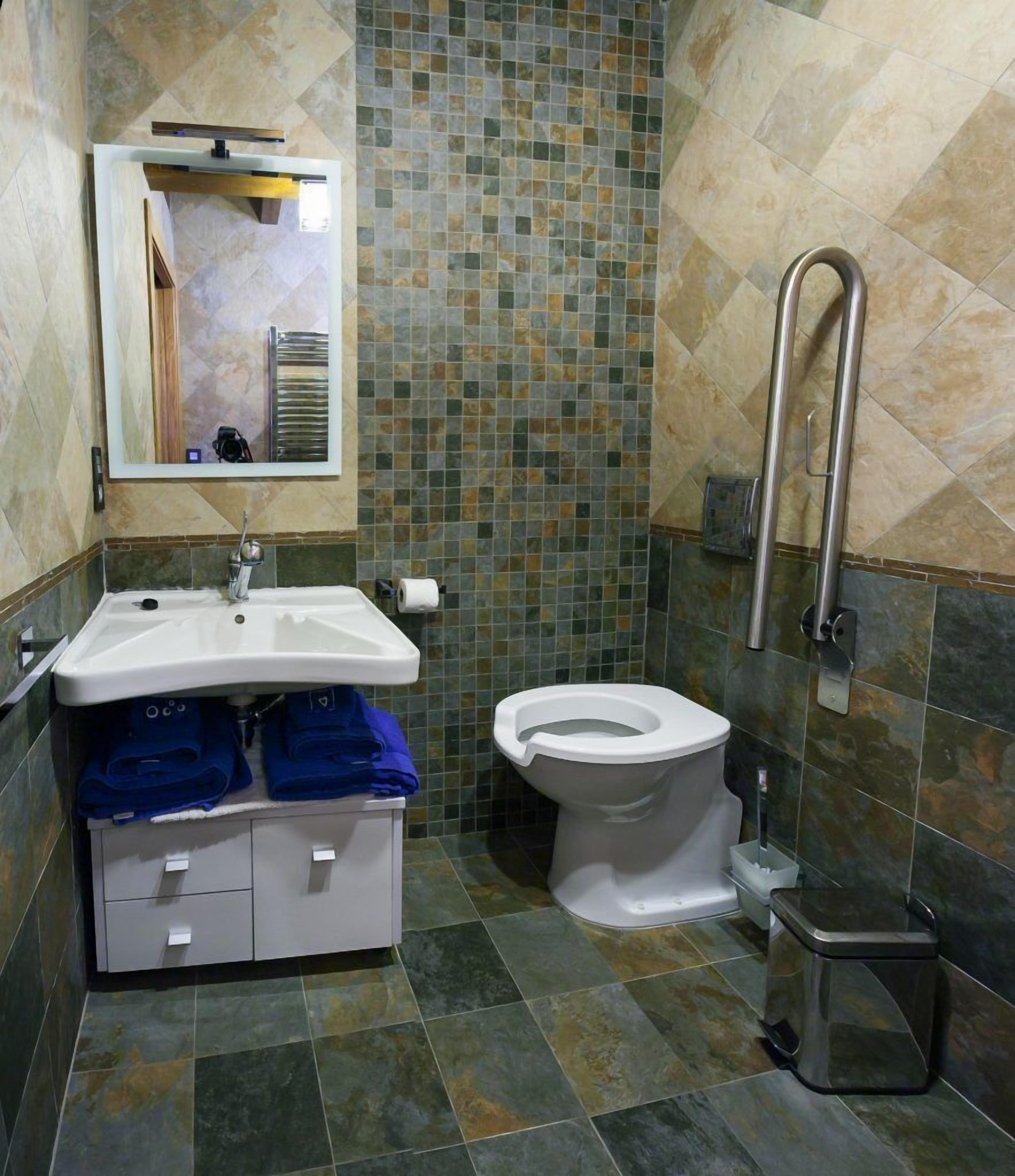 Une salle de bain avec un lavabo blanc, des toilettes et un miroir. Il y a des serviettes bleues sur le lavabo et une poubelle à côté des toilettes.