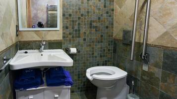 Une salle de bain avec un lavabo blanc, des toilettes et un miroir. Il y a des serviettes bleues sur le lavabo et une poubelle à côté des toilettes.