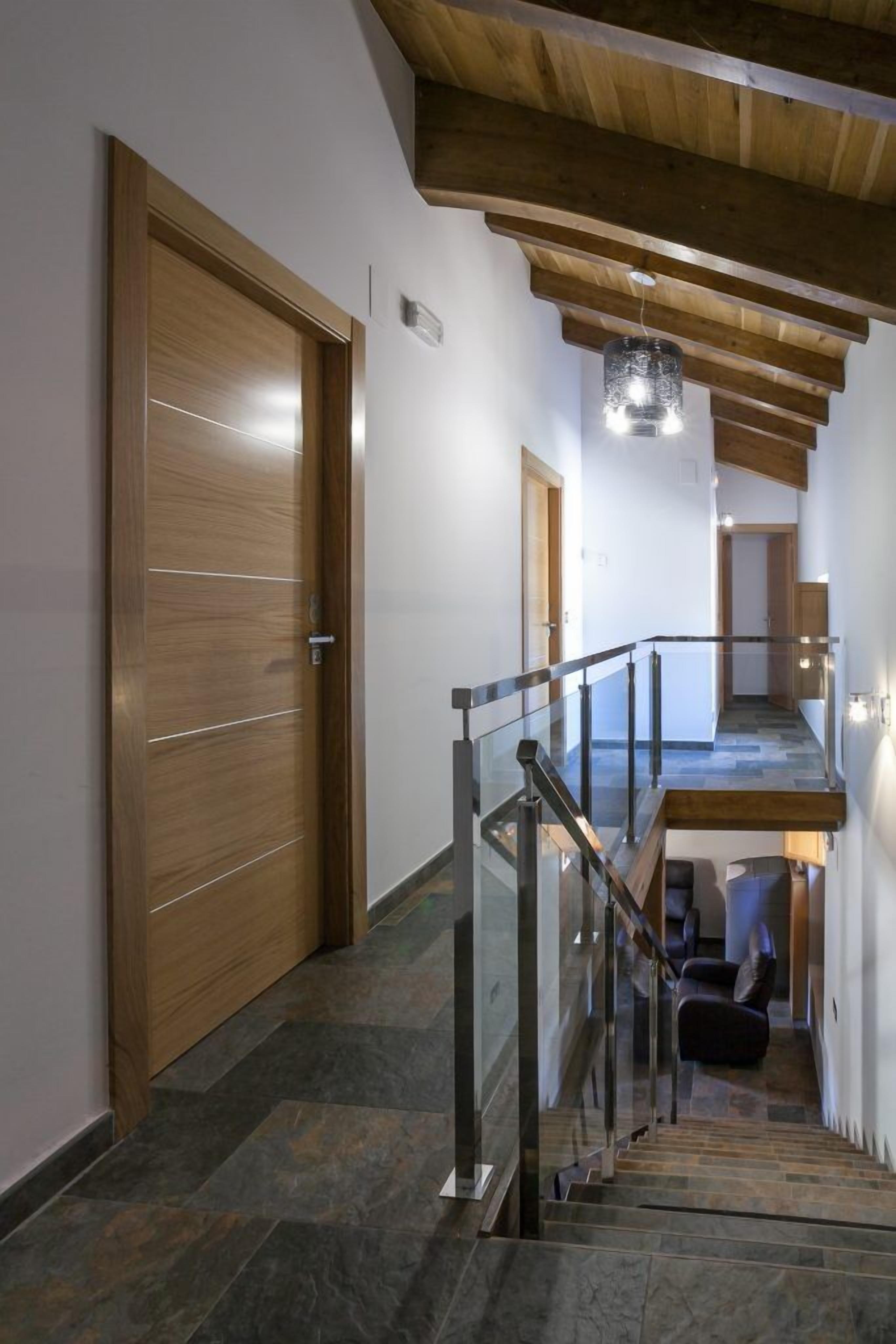 Un intérieur moderne avec une porte en bois, un escalier doté de rampes en verre et un luminaire suspendu.