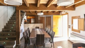 A spacious dining area with a long table and chairs, a staircase with directional arrows, and a kitchen area in the background. - El Abrigaño del Cañon I y II (Valle de Sedano)