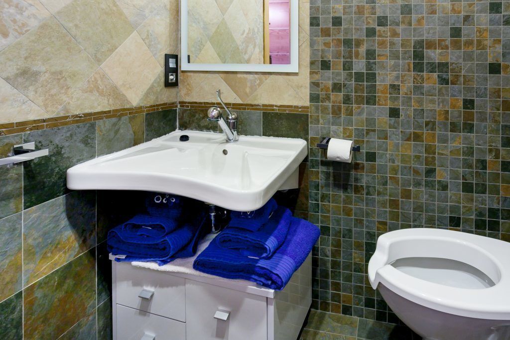 Et badeværelse med en hvid vask, blå håndklæder, et toilet og et spejl over vasken.