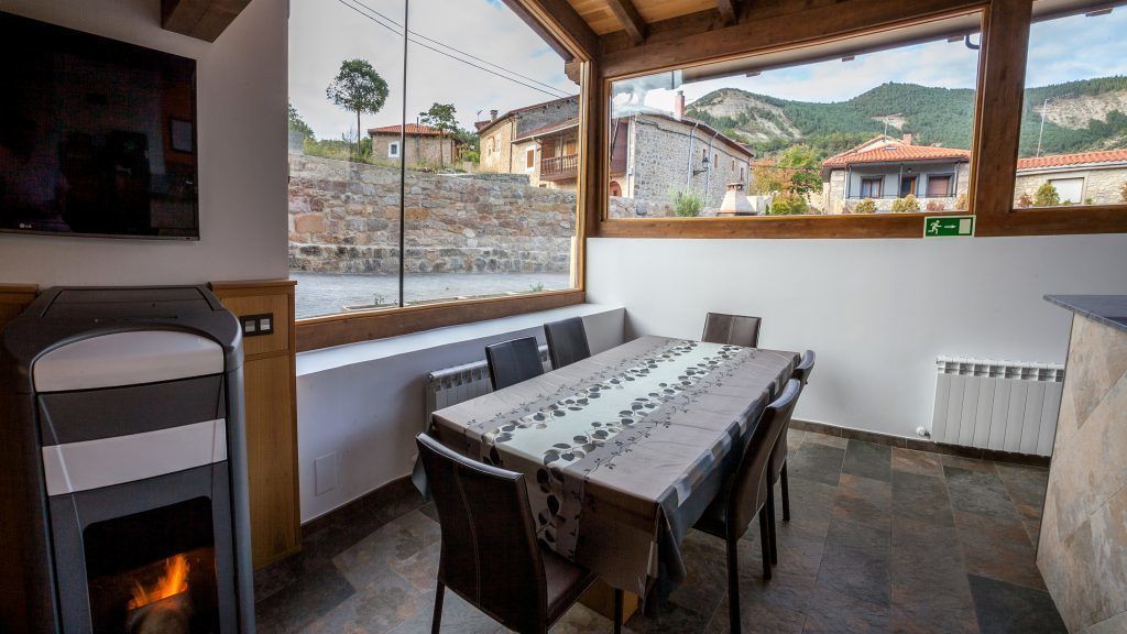 A dining area with a long table, chairs, a fireplace, and a view of the village through large windows.