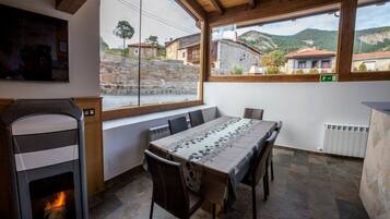 Un espace repas comprenant une longue table, des chaises, une cheminée et une vue sur le village, grâce à de grandes fenêtres.