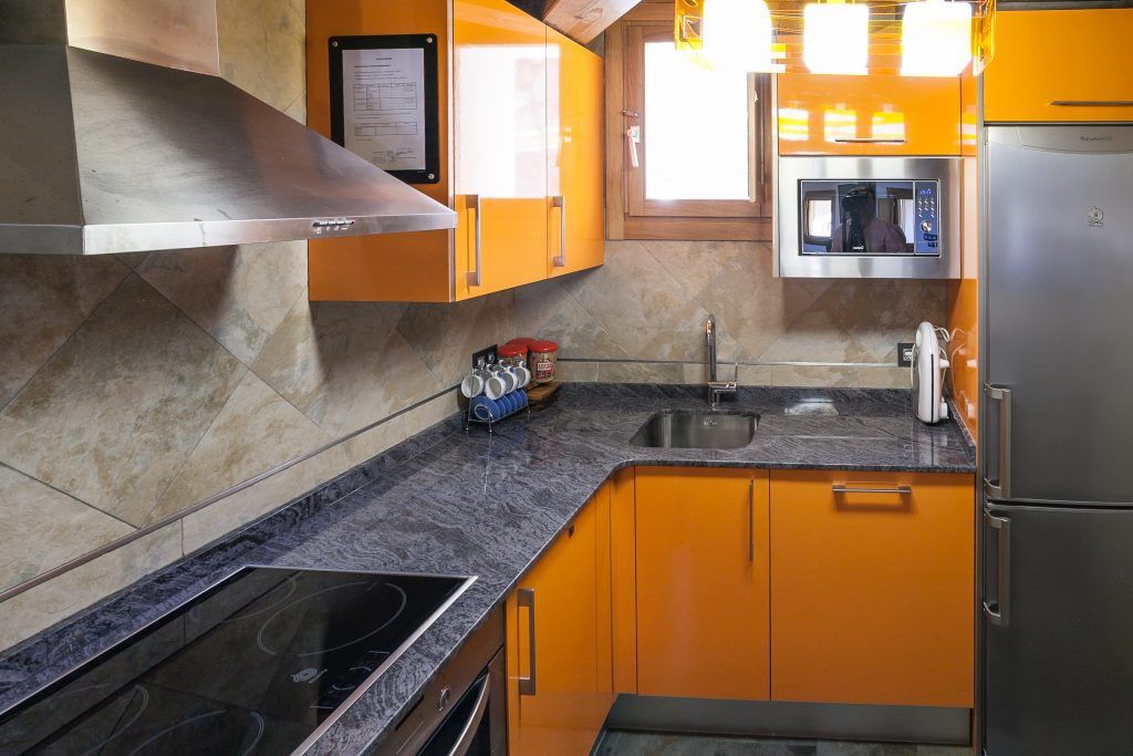 A kitchen with orange cabinets, a stainless steel range hood, a microwave, and a refrigerator.