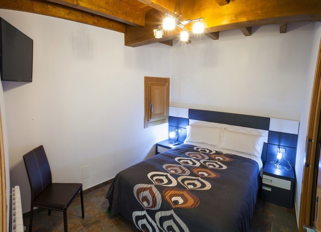 A bedroom with a bed, a chair, a nightstand, and a wooden ceiling.