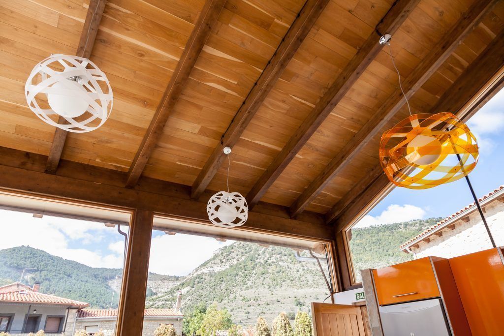 Techo de madera con lámparas esféricas colgantes y vista a un paisaje montañoso a través de amplios ventanales.