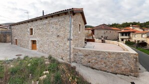 A stone building with a small porch and a door, surrounded by a stone wall and a paved area. - El Abrigaño del Cañon I y II (Valle de Sedano)