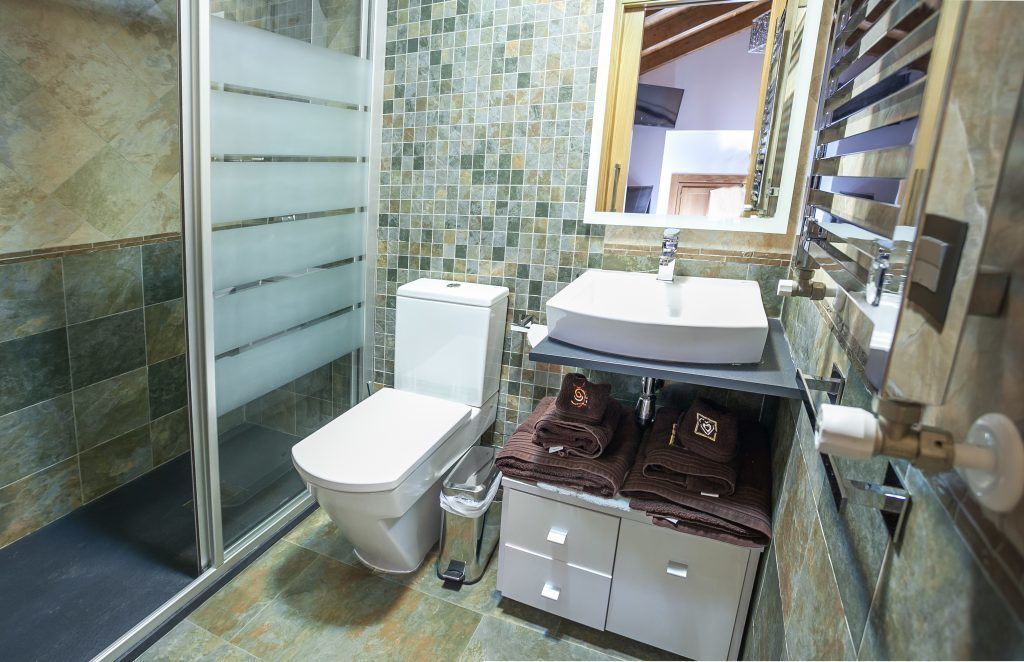A bathroom with a glass shower enclosure, a toilet, a sink with a mirror, and a towel rack with towels.