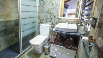 A bathroom with a glass shower enclosure, a toilet, a sink with a mirror, and a towel rack with towels.