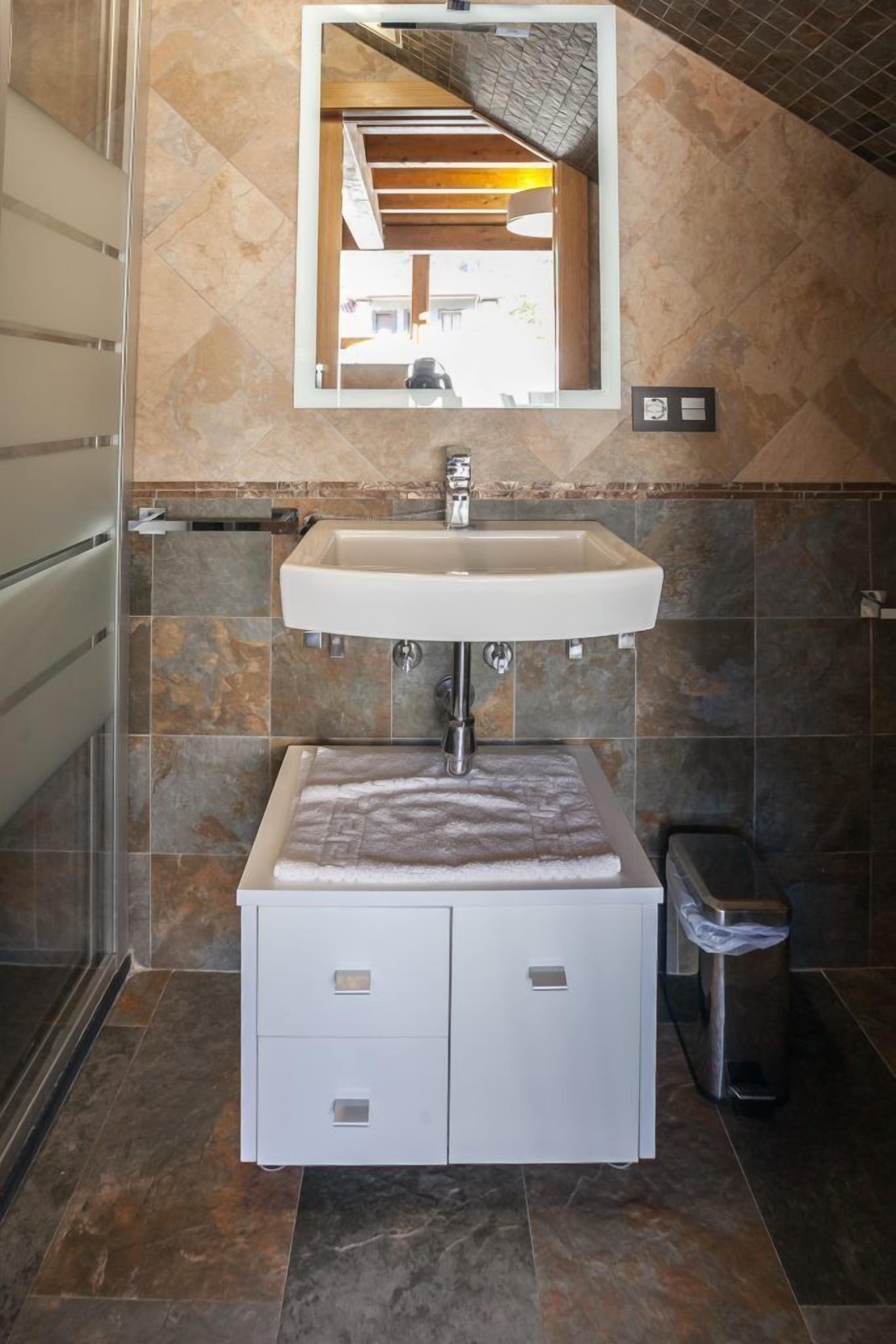 Un baño moderno con un lavamanos blanco, un espejo encima y suelo de baldosas.