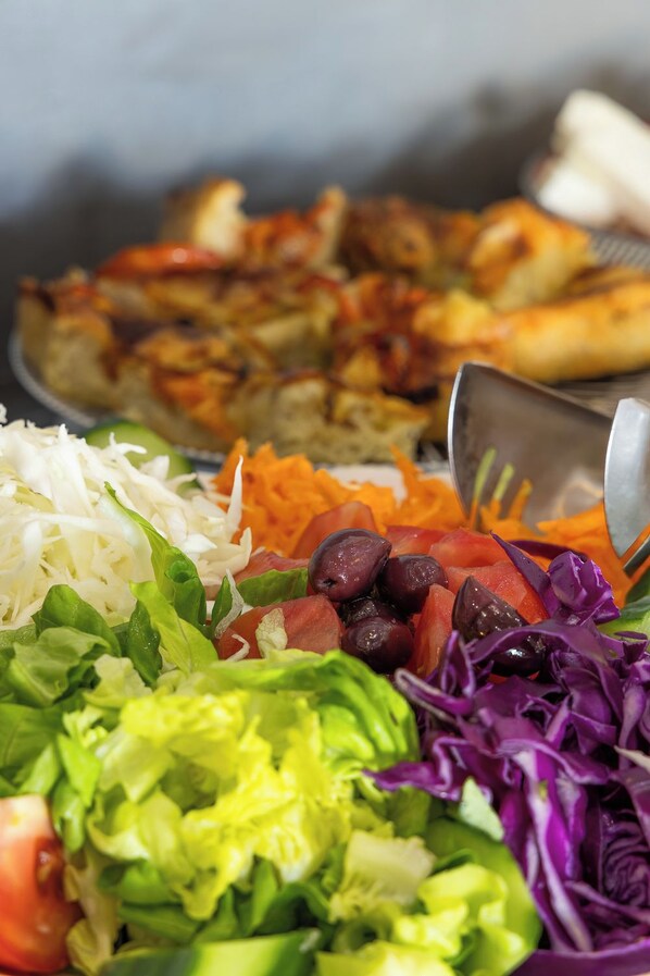 A variety of food items including a salad with lettuce, tomatoes, and olives, and a pizza with visible toppings. - Hotel Almira (Pineios)