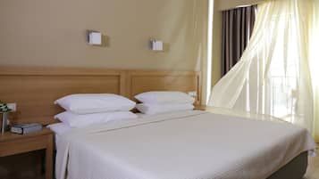 A neatly made bed with white bedding, a wooden headboard, and a nightstand with a book and a vase of flowers.