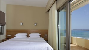 A hotel room with a large bed, a nightstand, a glass door leading to a balcony with a view of the sea. - Hotel Almira (Pineios)