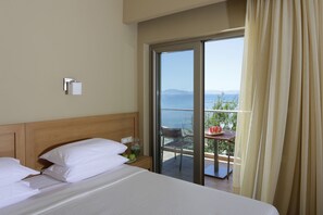 A hotel room with a bed, a nightstand, a table with a glass of water, and a view of the sea through a sliding glass door.