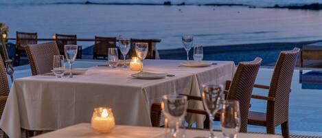 A table set for dining with a view of the ocean at dusk.