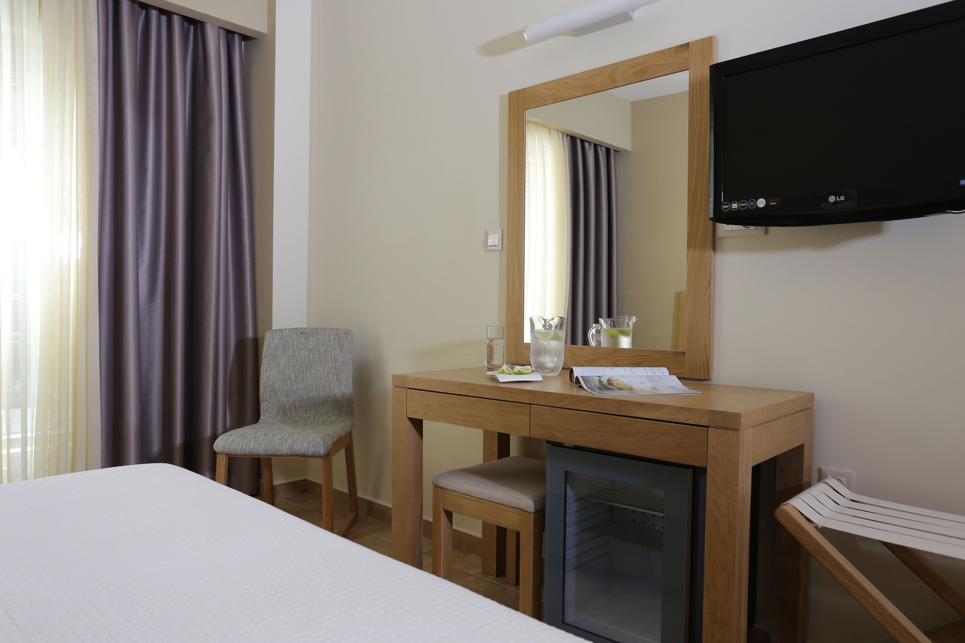 A hotel room with a bed, a wooden desk with a mirror, a television, and a chair.