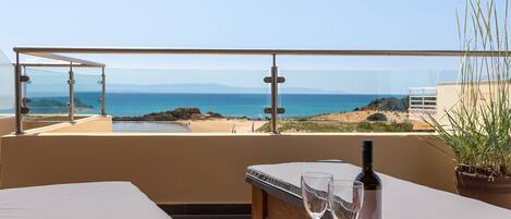 A terrace with a table, two glasses, and a bottle of wine, overlooking a beach and the sea.