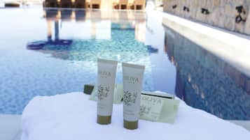 Zona de piscina con dos botellas de productos OLIVA sobre una toalla blanca.