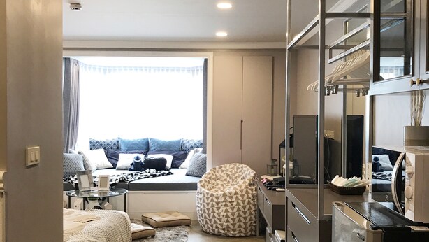A compact bedroom with a bed, a seating area with a sofa and pillows, a small table, and a kitchenette. - Stay in Style Family Room at Nimman R201 (Chiang Mai)