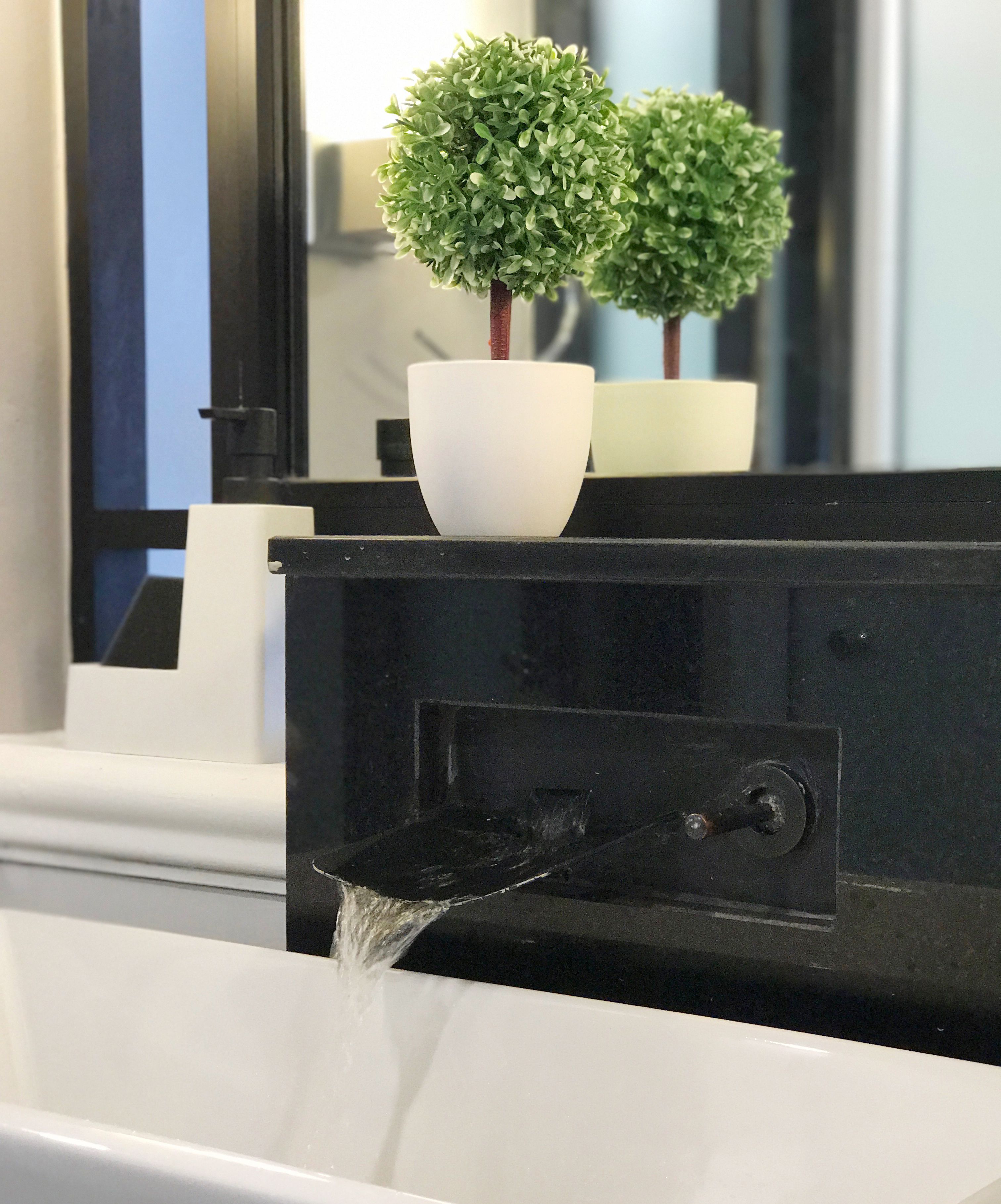 Un baño con un lavamanos blanco, una pequeña planta en maceta y un grifo negro.
