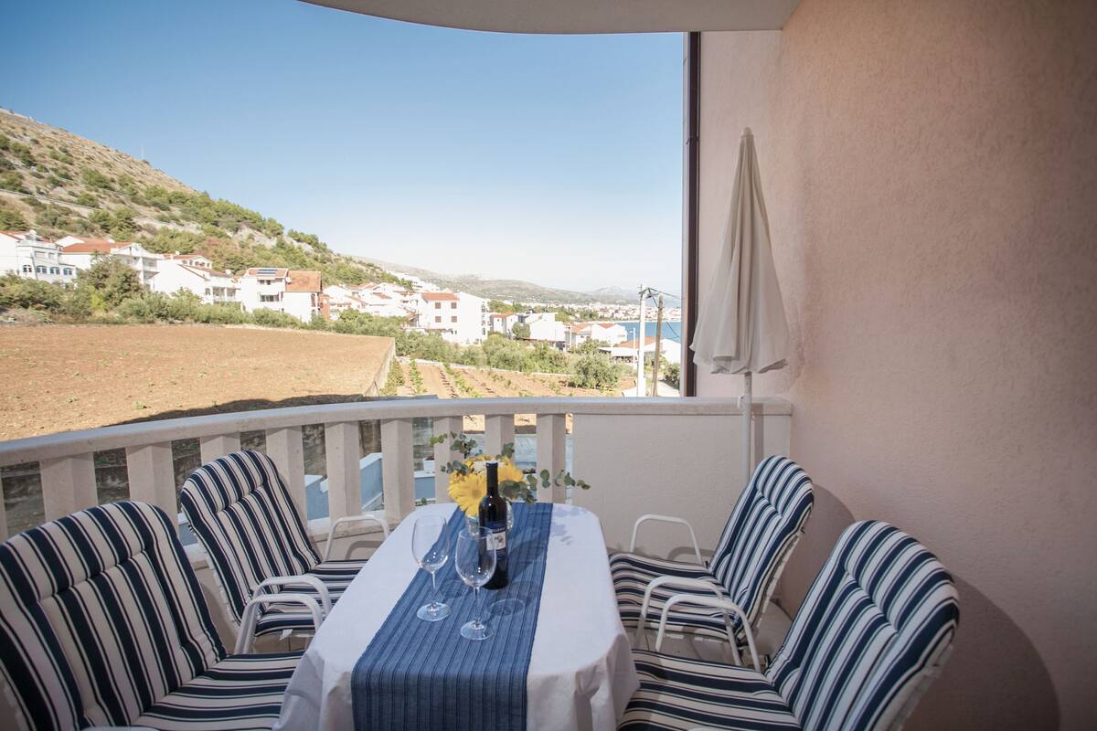 A balcony with a table set for two, featuring striped chairs and a bottle of wine.