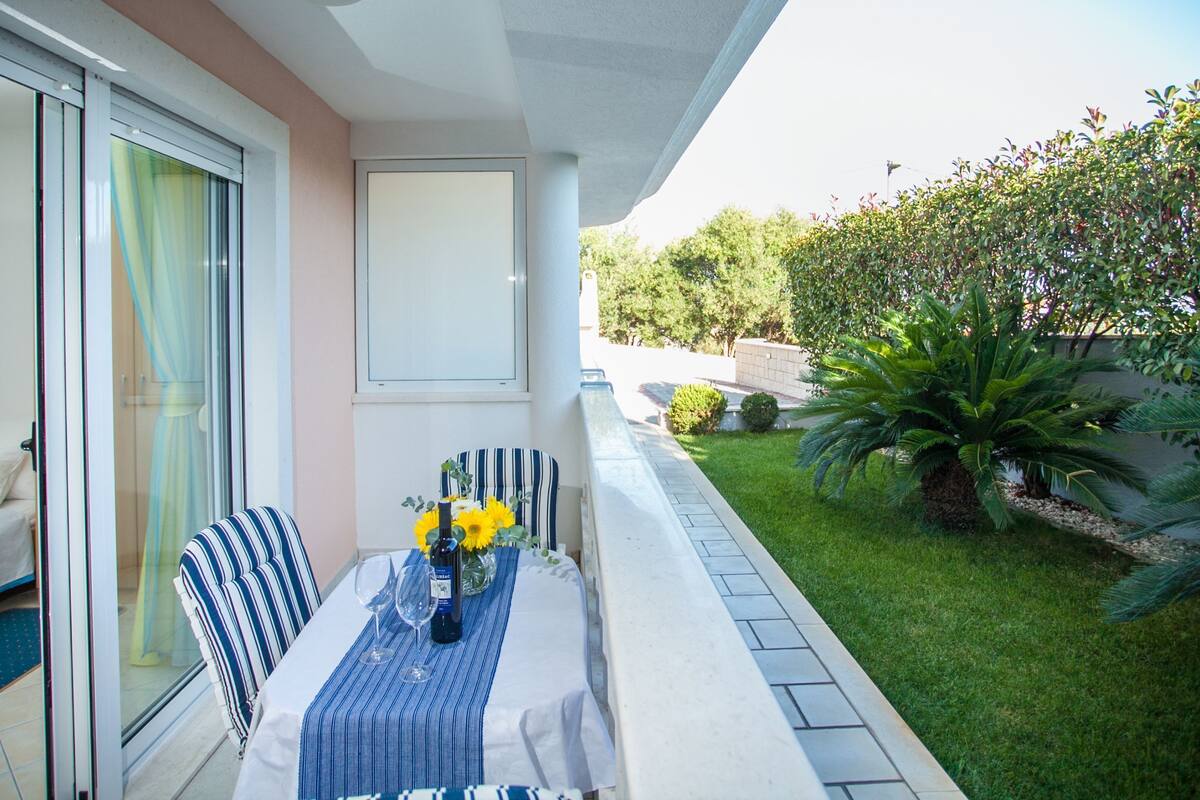 A balcony with a table set for two, featuring a striped chair and a vase with sunflowers.