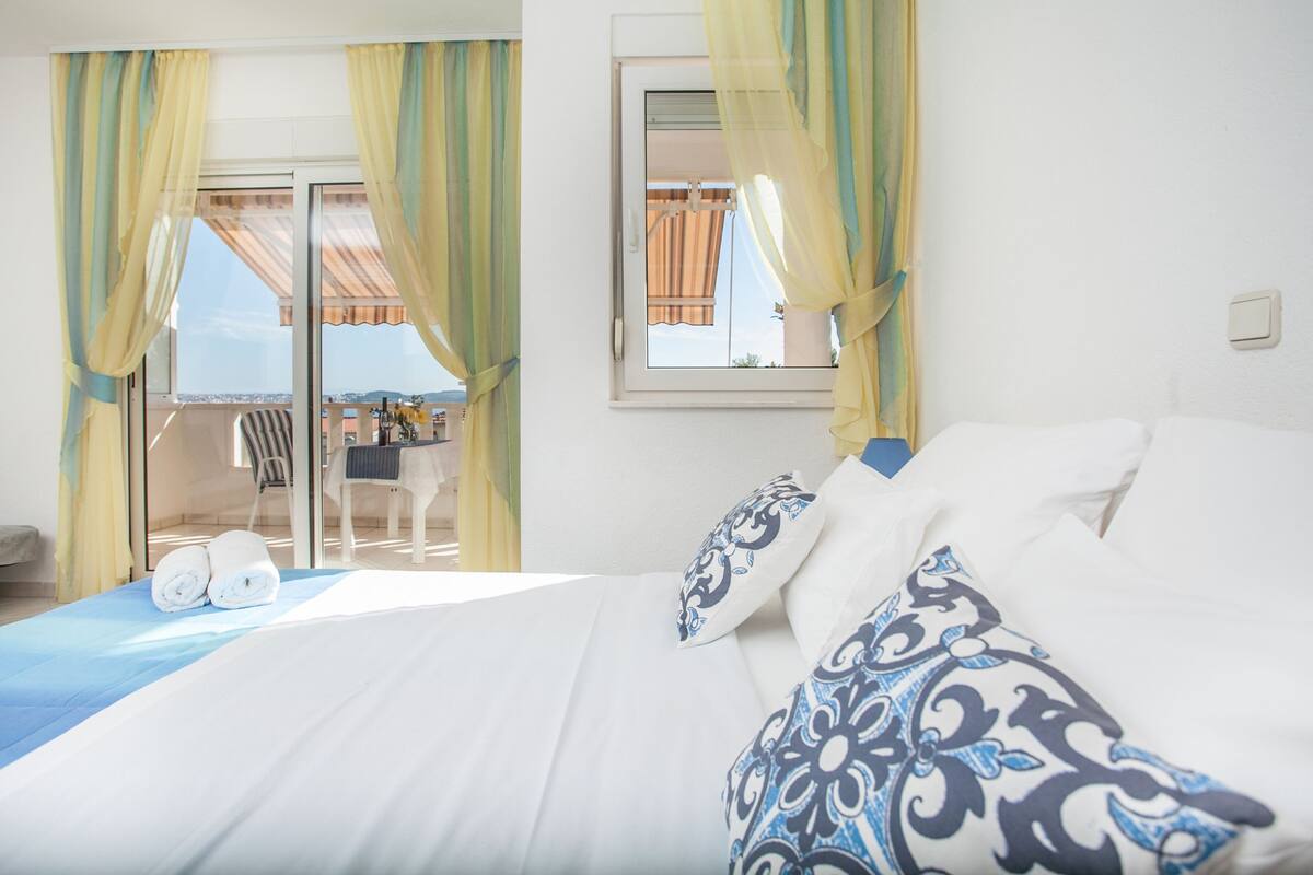 A hotel room with a bed, a window with curtains, a view of the outside, and a table with chairs.