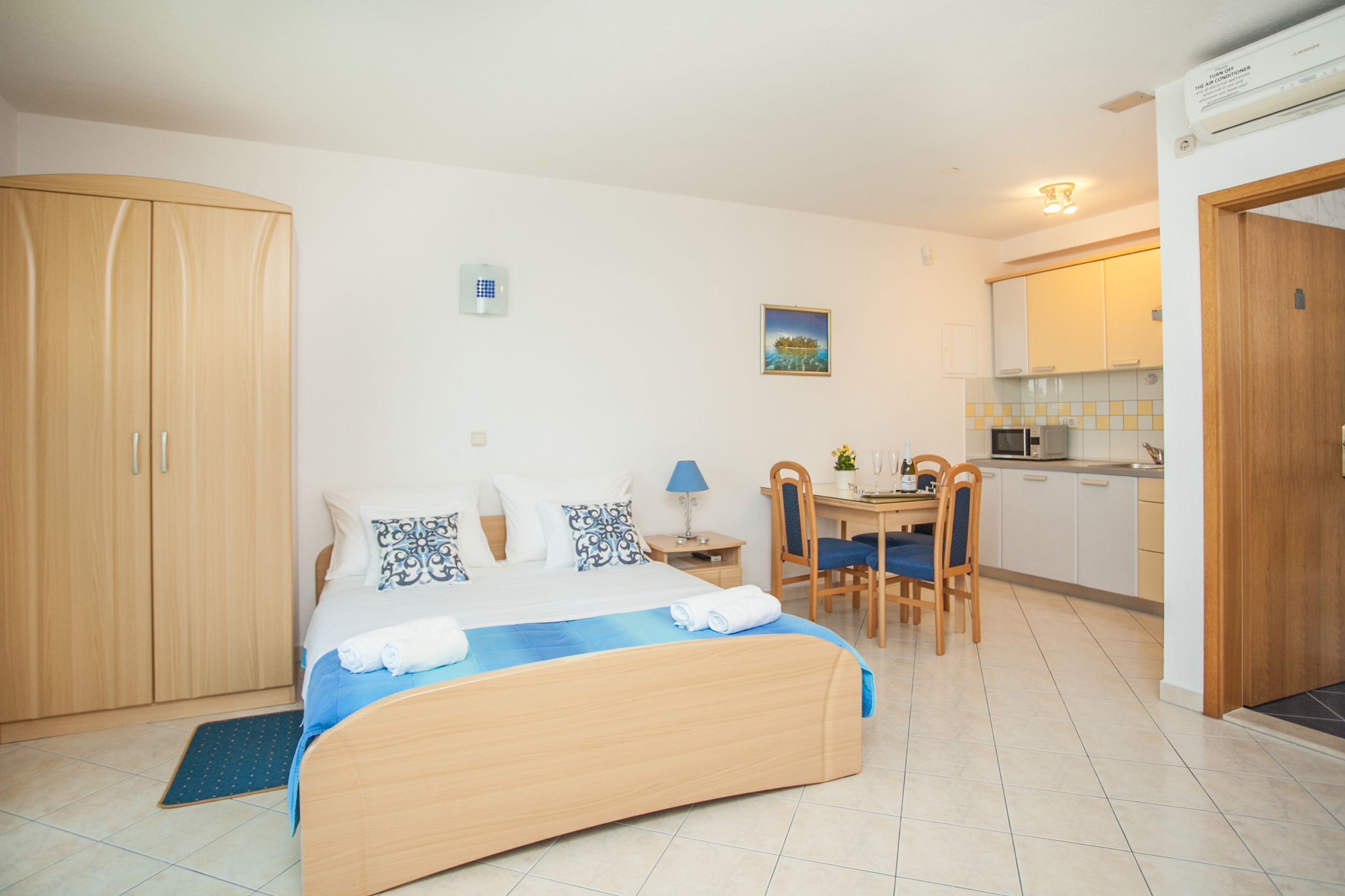 A bedroom with a bed, a desk, and a kitchenette.