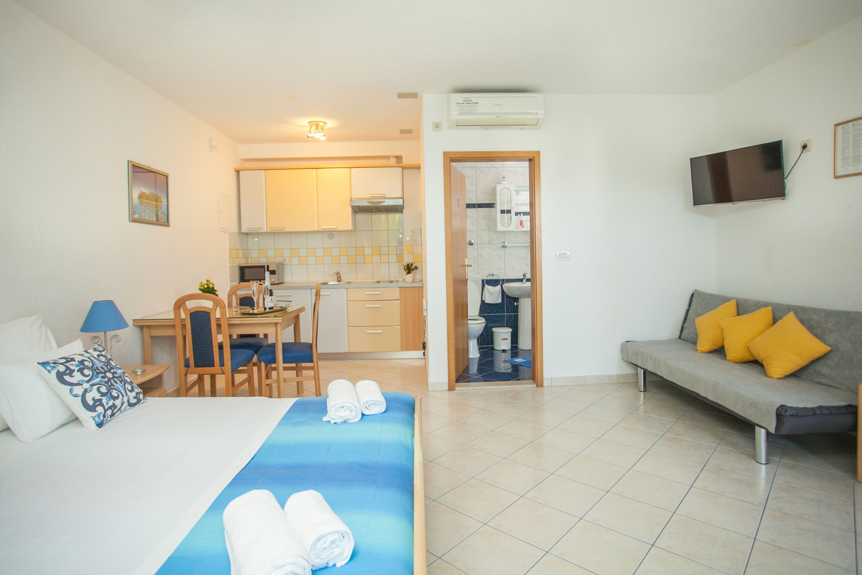 A hotel room with a bed, a sofa, a dining area, and a bathroom.