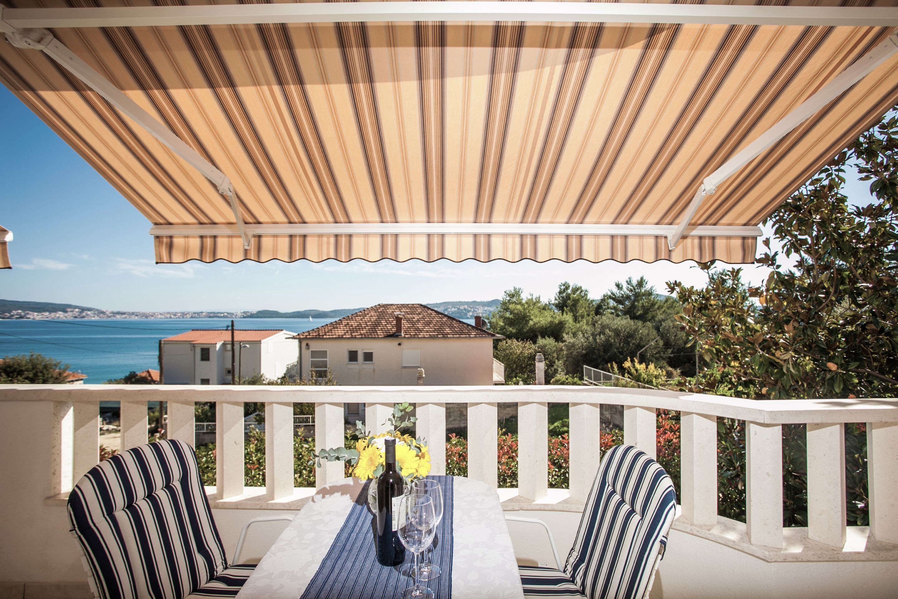 Una terraza con una mesa, sillas a rayas y vistas al mar y edificios.