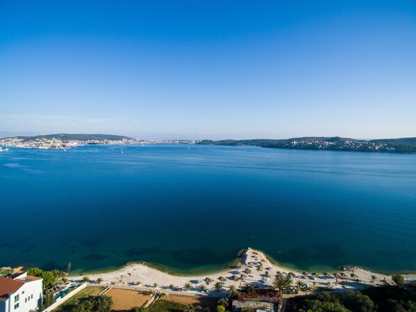A coastal view with a clear blue sea, a sandy beach, and a small town in the distance. - Apartments Barbara (Seget)