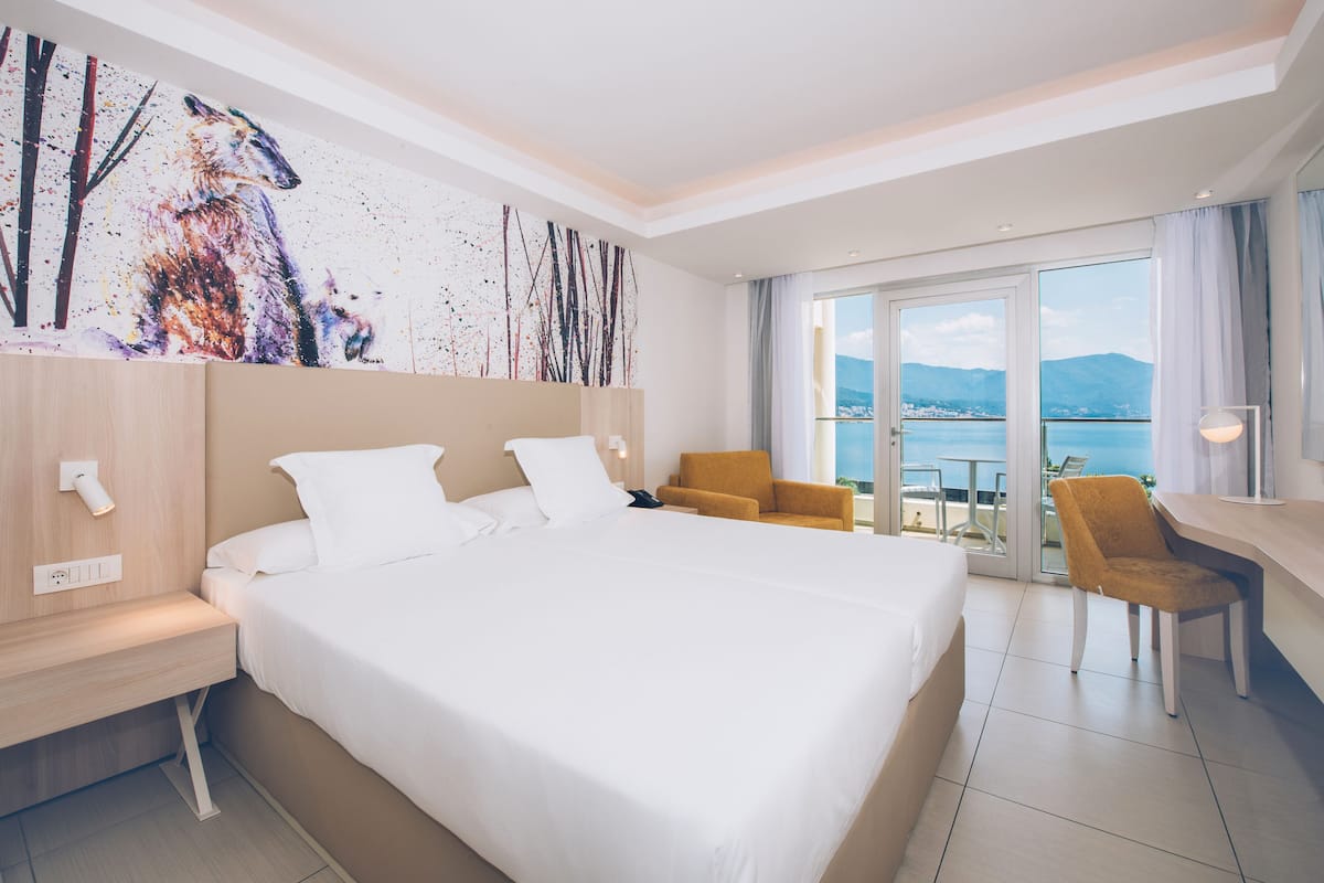 Quarto de hotel com uma cama grande, uma escrivaninha, uma cadeira e vista para o mar.