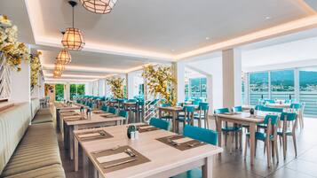 Ein modernes Restaurant mit langen Gemeinschaftstischen und Sitzgelegenheiten, große Fenster mit Blick auf die Stadt und dekorative Blumenarrangements.