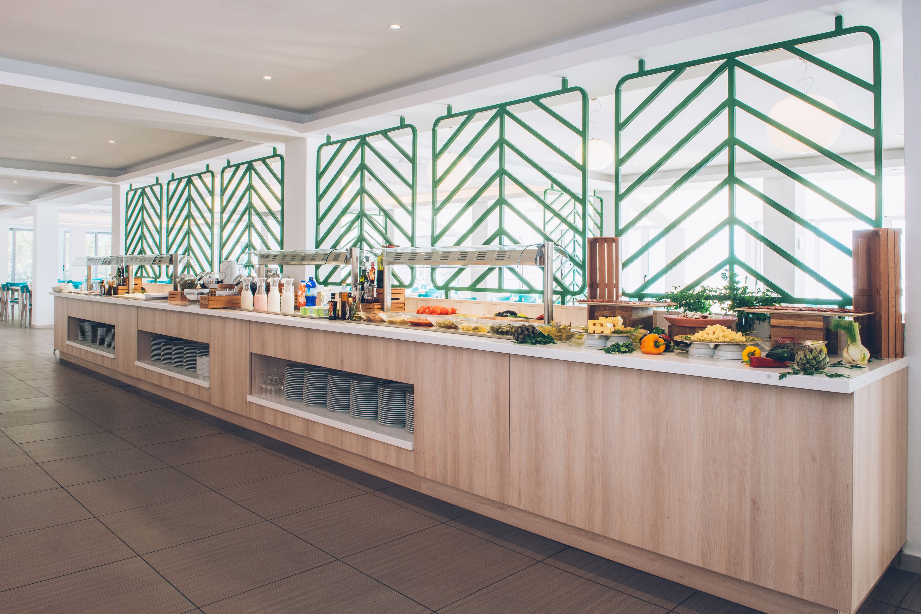 Zona de buffet con una larga barra, diferentes opciones de comida y un separador con diseño de chevron verde.