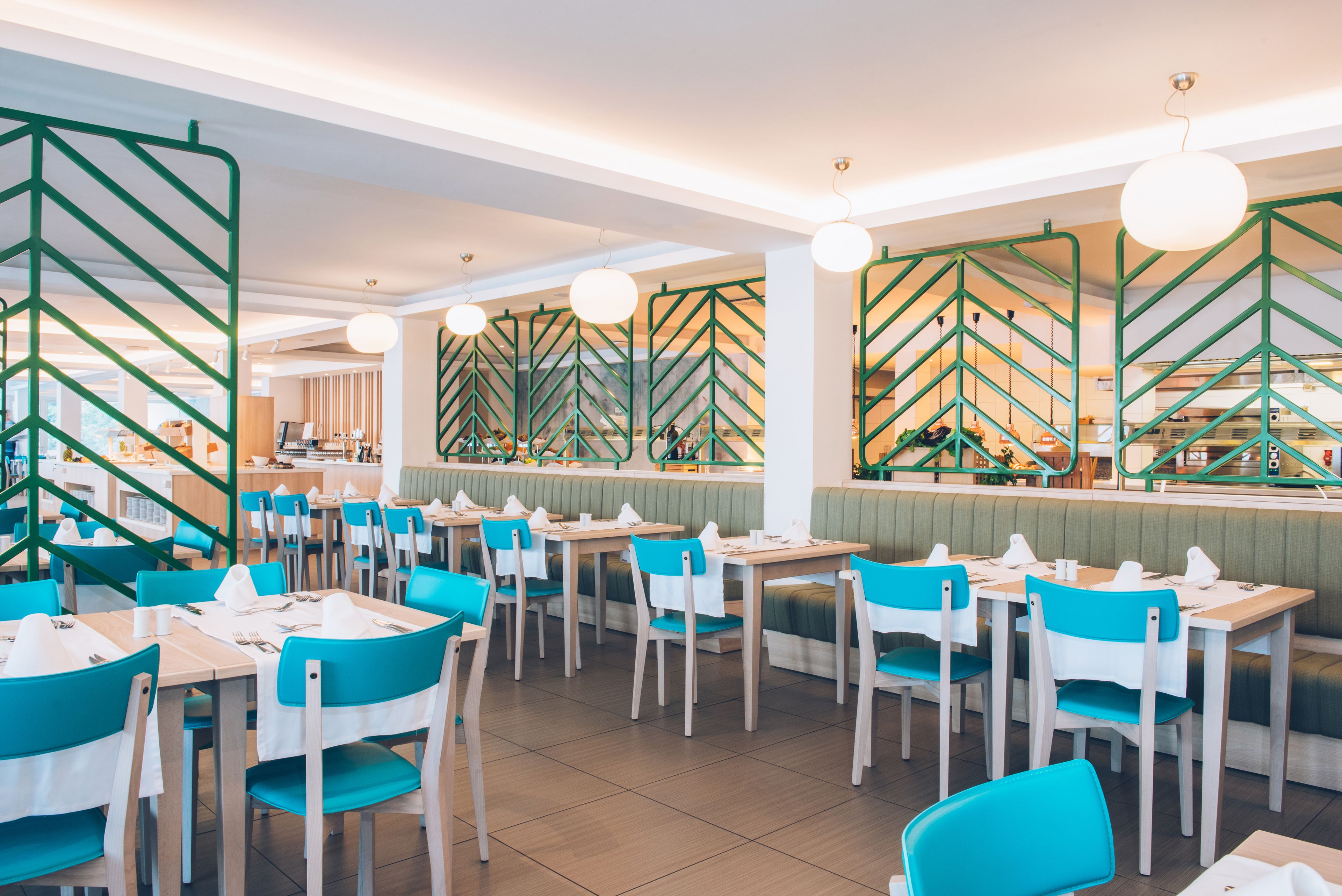 A restaurant with multiple tables and chairs, a counter area, and a green decorative wall.