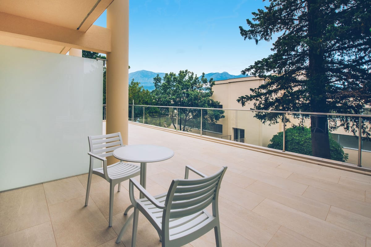Varanda com duas cadeiras e uma mesa, com vista para uma montanha e árvores.