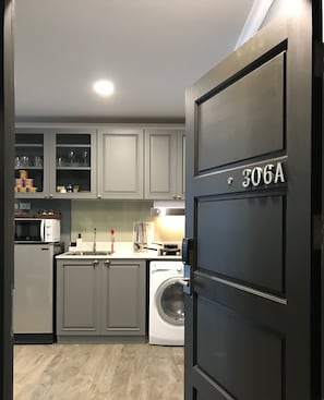 A compact kitchen with grey cabinets, a washing machine, a microwave, and a sink.