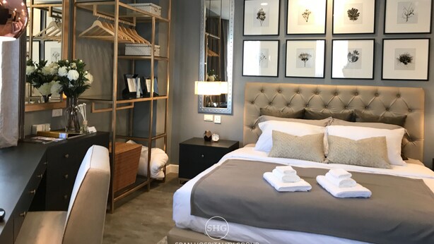 A hotel room with a large bed, a wardrobe, a desk, and a mirror. There are framed pictures on the wall and a vase with flowers on the desk. - Stay in Style The Heart of Nimman R306A (Chiang Mai)