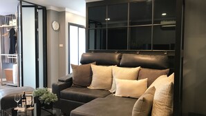 A modern living room with a leather sofa, a glass coffee table, and a large window. - Stay in Style The Heart of Nimman R306A (Chiang Mai)